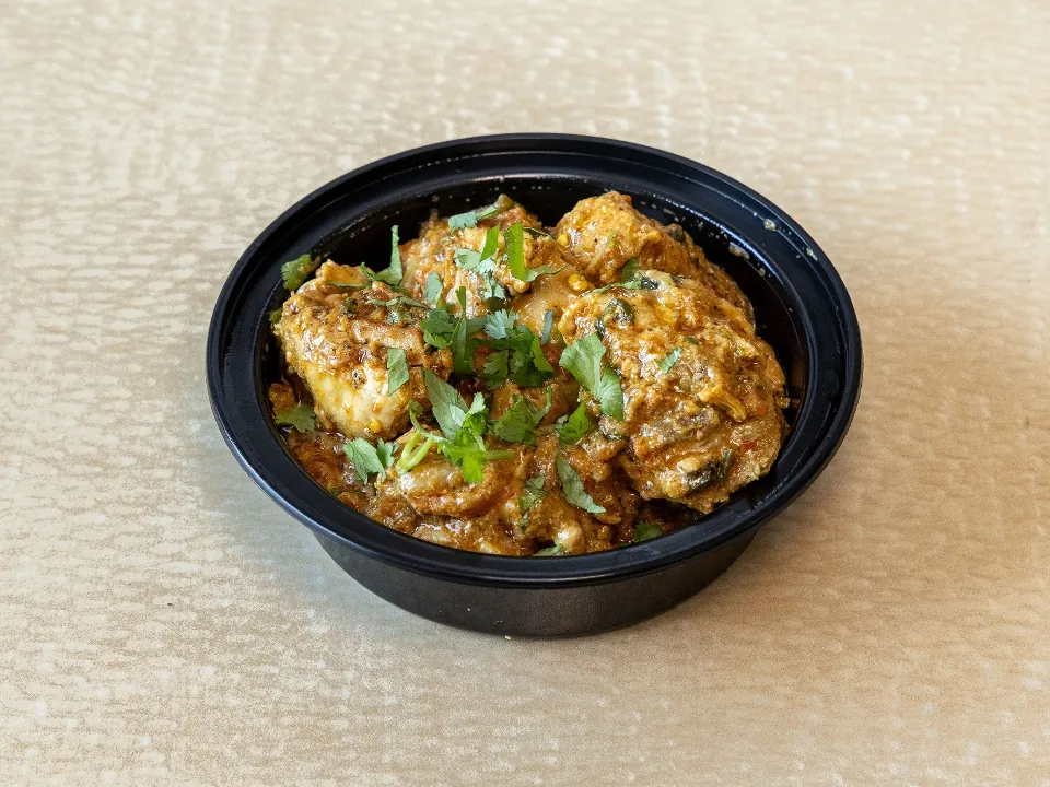 Chicken karahi in a takeout bowl, topped with cilantro and ginger