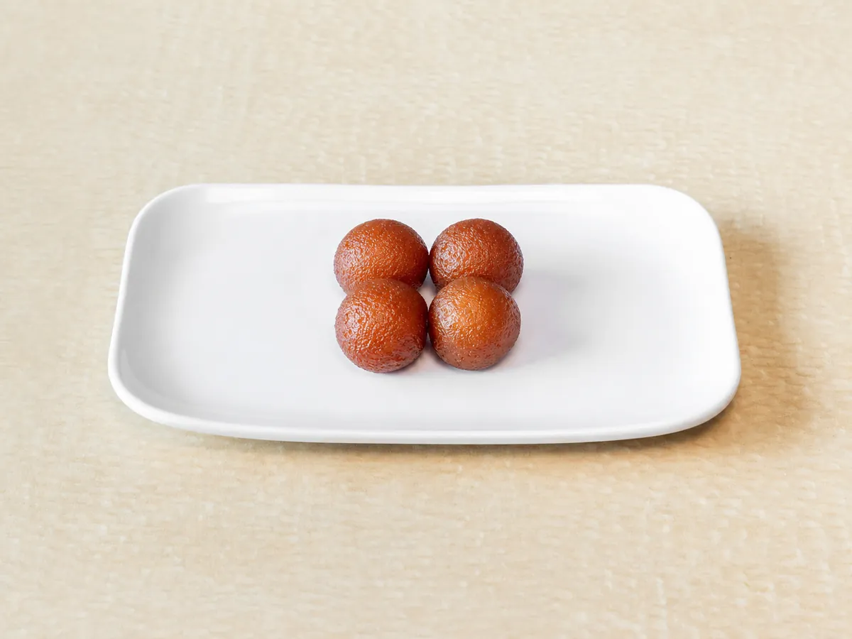 Four gulab jamun on a white plate